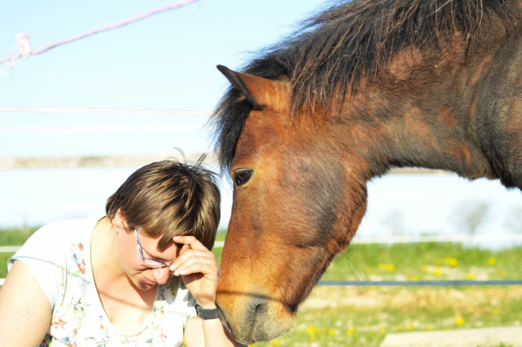 Une humaine tête baissée et la tête d'un poney au regard doux près d'elle